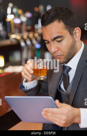 Serious businessman working on his tablet computer while having a whisky Stock Photo