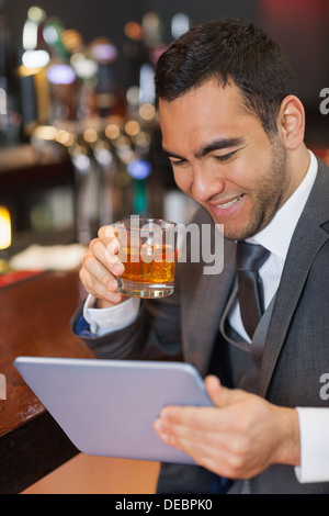 Smiling businessman working on his tablet while having a whiskey Stock Photo