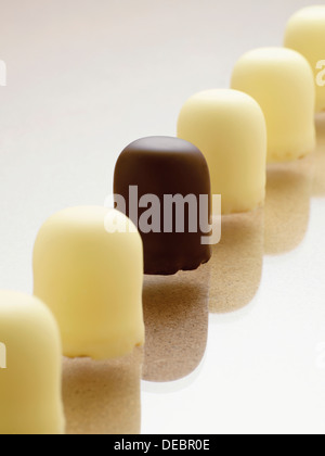 Row of chocolate-coated marshmallow treats with white chocolate, a single one with dark chocolate Stock Photo