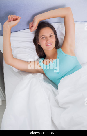 Brunette woman stretching and smiling in bed Stock Photo