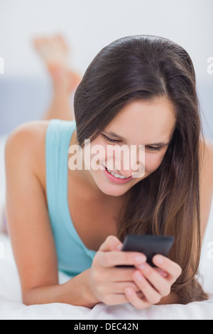 Woman using her phone and smiling while on the bed Stock Photo