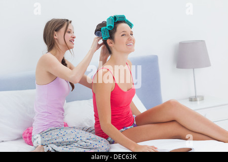 Girls sitting in bed one wearing hair rollers Stock Photo