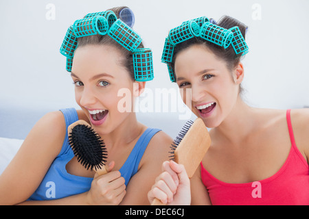 Friends in hair rollers singing into their hairbrushes Stock Photo