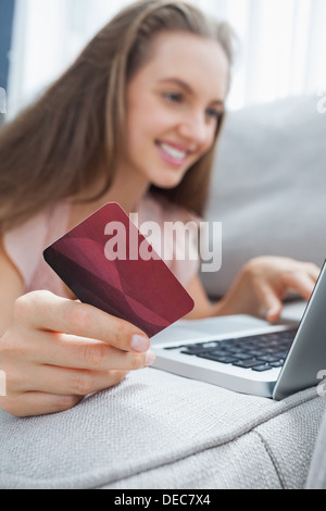 Smiling woman lying ona sofa holding a card and laptop Stock Photo