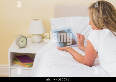 Thoughtful woman using a tablet pc lying on her bed Stock Photo