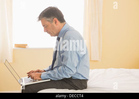 Concentrated man using a laptop sitting on bed Stock Photo