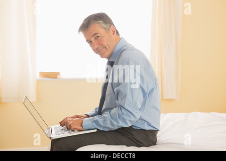 Thoughtful man using a laptop sitting on a bed Stock Photo
