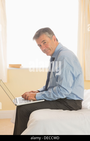 Focused man using a laptop sitting on a bed Stock Photo