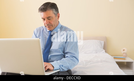 Thoughtfulman using a laptop sitting on a bed Stock Photo