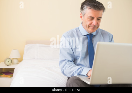 Thoughtful man using a laptop sitting on a bed Stock Photo