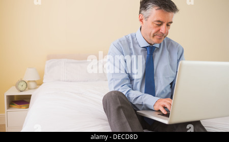 Concentrated man using a laptop sitting on a bed Stock Photo