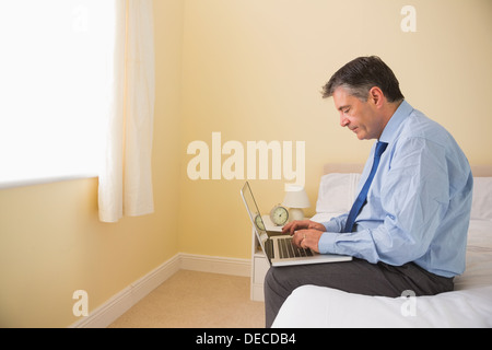 Focused man using a laptop sitting on a bed Stock Photo