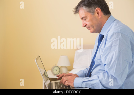 Focused man using a laptop sitting on a bed Stock Photo