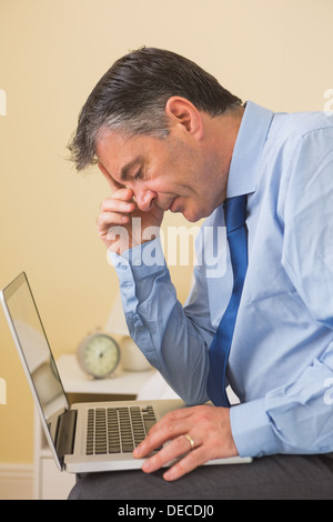 Tired man using a laptop sitting on a bed Stock Photo