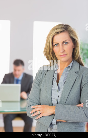 Serious businesswoman looking at camera crossed arms with a businessman working on background Stock Photo
