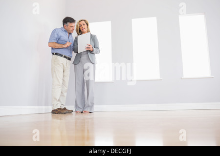 Concentrated blonde realtor showing a room and some documents to a potential attentive buyer Stock Photo