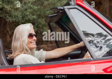 Happy mature woman with sunglasses driving red convertible Stock Photo