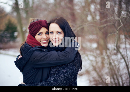 Friends hugging each other on a bright winter day with white snow on background Stock Photo