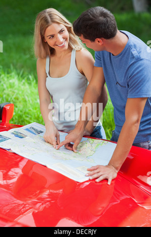 Smiling young couple reading map on their cabriolet bonnet Stock Photo