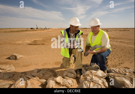 Geologists on surface gold mine examining core and grade samples from exploration drill rigs seen behind, Mauritania, NW Africa Stock Photo