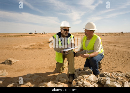 Geologists on surface gold mine examining core and grade samples from exploration drill rigs seen behind, Mauritania, NW Africa Stock Photo