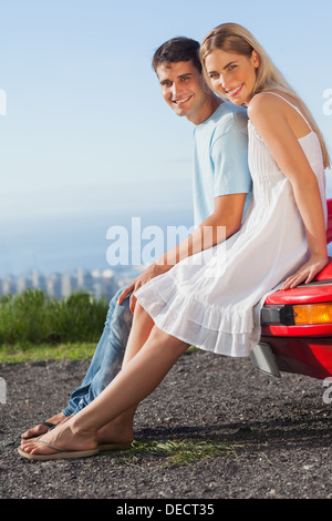 Happy couple sitting on their cabriolet car hood Stock Photo