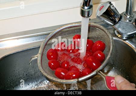 Red Cherry Tomatoes being rinsed under running tap water Stock Photo