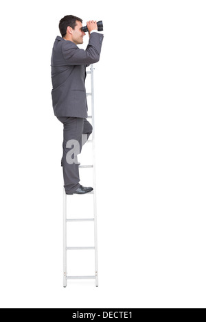 Businessman standing on ladder using binoculars Stock Photo