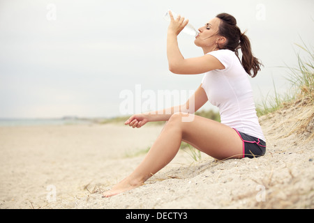 Active fitness woman at the beach drinking water from bottle.