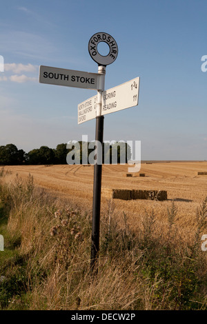 Old cast iron Oxfordshire road sign, a field of straw bales behind. Stock Photo