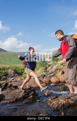 Man helping his girlfriend to cross a stream Stock Photo
