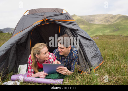 Happy couple lying in their tent and using digital tablet Stock Photo