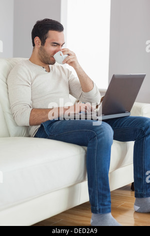 Relaxed attractive man drinking coffee while working on his laptop Stock Photo