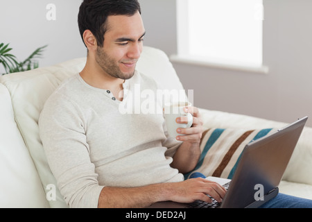 Calm attractive man drinking coffee while working on his laptop Stock Photo