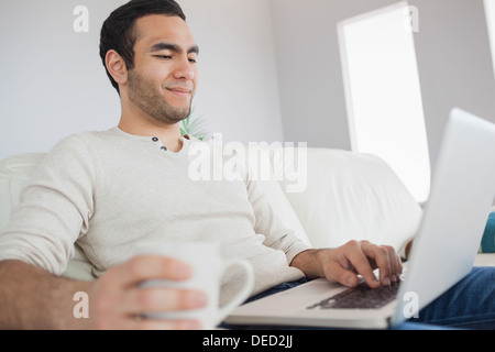 Peaceful handsome man having coffee while using his laptop Stock Photo