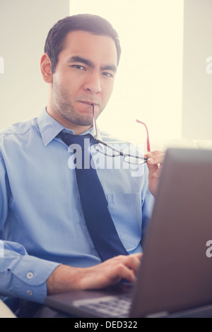 Irritated man biting his eyeglasses and using a laptop Stock Photo