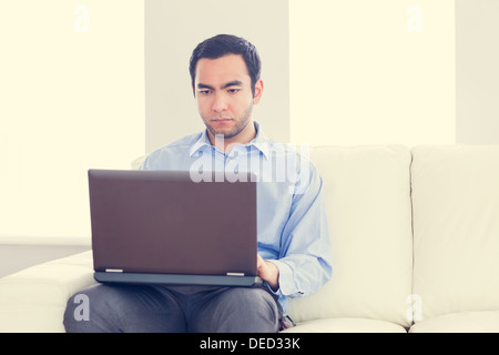 Bored man using a laptop sitting on a sofa Stock Photo