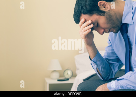 Sad man sitting head in hands on his bed Stock Photo