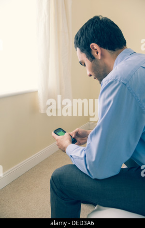 Man using a mobile phone sitting on a bed Stock Photo