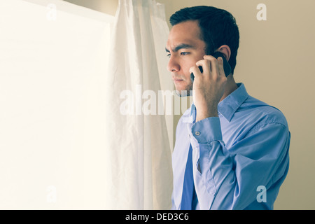 Irritated man calling someone with a mobile phone and looking out the window Stock Photo