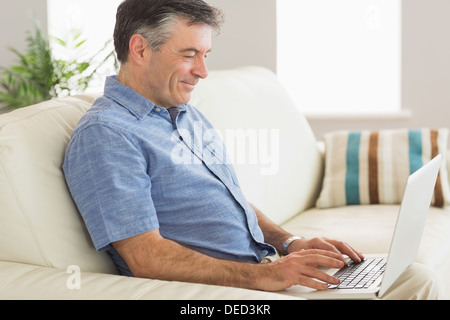 Smiling man sitting on a sofa using a laptop Stock Photo