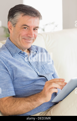 Smiling man sitting on a sofa using a tablet pc Stock Photo