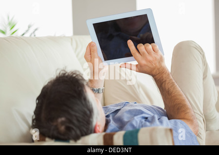 Man laying on sofa using a tablet pc Stock Photo