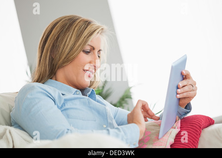 Smiling woman lying on sofa using a tablet pc Stock Photo