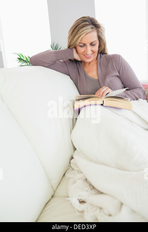Smiling woman reading a book on a sofa Stock Photo