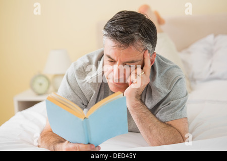 Concentrated man reading a book on his bed Stock Photo