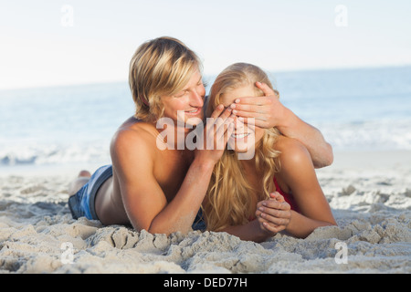 Man covering girlfriends eyes lying on the beach Stock Photo