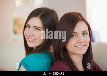 Two happy friends sitting back-to-back on the sofa Stock Photo