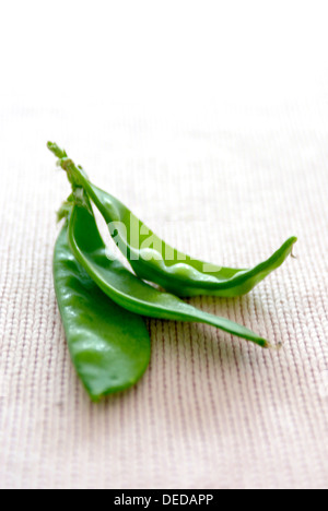 Three fresh snow pea pods on a fabric surface. Stock Photo