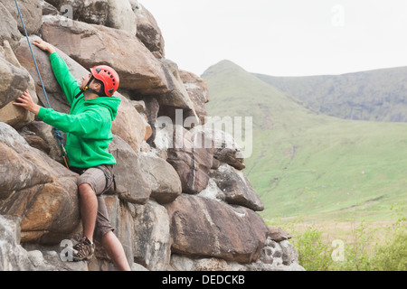 Focused man scaling a large rock face Stock Photo